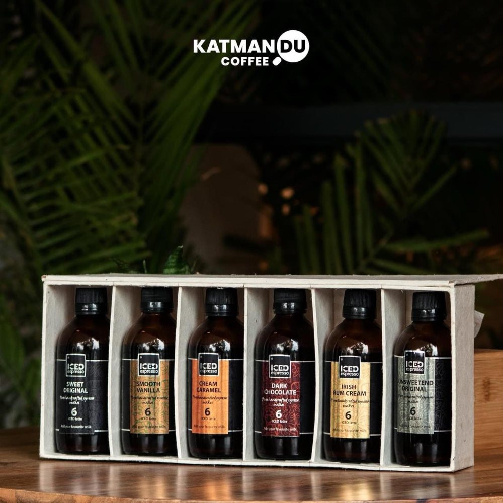 Set of Katmandu Coffee bottles in a wooden crate with a blurred greenery background.